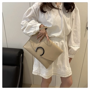 Detail of beige envelope clutch bag featuring a black metal C-shaped buckle and wrist strap