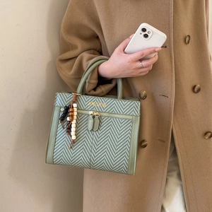 Detail of dark green herringbone handbag with beaded tassel and golden logo