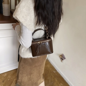 Sac boîte vintage en cuir verni marron foncé avec poignée porté par un mannequin chic
