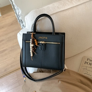 Vintage black tote bag in pebbled leather with wood bead charm on a beige sofa