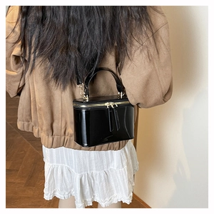 Detail of a black patent leather box bag with gold-tone hardware on a model back view