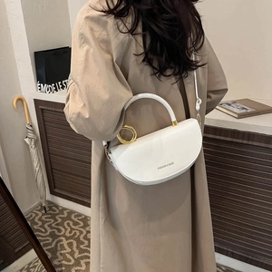 Elegant white semi-circle saddle bag with gold ring hardware shown on a beige trench coat