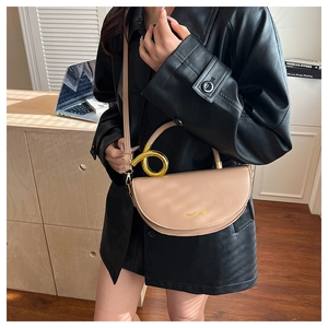 Detail of beige saddle bag with gold ring handle and logo on black leather jacket