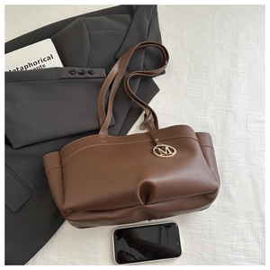 Detail of dark brown PU leather tote bag with gold M charm and side pocket texture