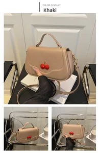 Detail of khaki leather crossbody bag featuring red cherry decor and gold hardware