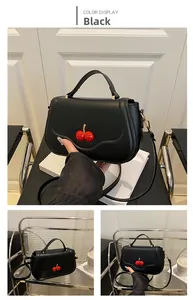 Detail of black matte leather shoulder bag with 3D red cherry decoration and strap