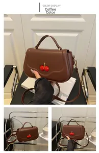 Detail of coffee brown leather handbag with metallic cherry charm and smooth finish