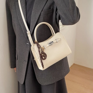 Chic cream leather square bag with litchi texture and brown charm worn by model