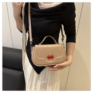 Detail shot of a beige cherry crossbody bag worn by a model in a minimalist setting