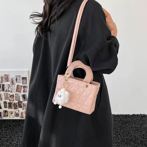 Sac à main rose matelassé avec bandoulière et pompon porté par un mannequin femme