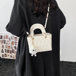 Sac fourre-tout matelassé blanc avec poignée et charm en peluche sur un manteau noir