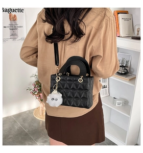 Détail du sac matelassé noir avec breloque ours blanc porté par un mannequin dans une pièce épurée