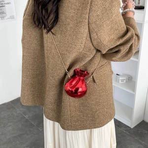 Glossy red metallic drawstring purse with gold chain strap worn by model in casual style