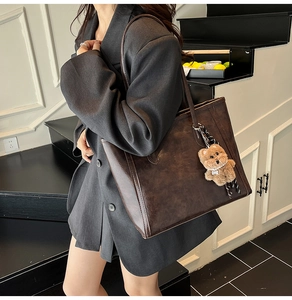 Detail of dark brown leather tote bag with a cute bear charm on a model's shoulder