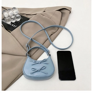 Close-up of a light blue crescent shoulder bag with elegant bow details and PU strap