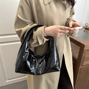 Classic black patent leather hobo bag with pleated texture worn by a model in a trench coat