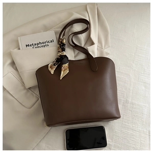 Detail der dunkelbraunen Leder-Shopper mit Seidenschal am Griff und Büro-Accessoires