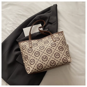 Close-up of monogram pattern tote bag with leather straps and gold rivet detailing