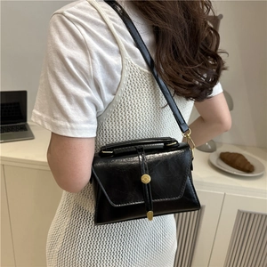 Borsa a tracolla nera lucida con fibbia dorata e manico indossata da una modella