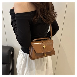 Brown vintage faux leather crossbody bag with round gold buckle shown on shoulder