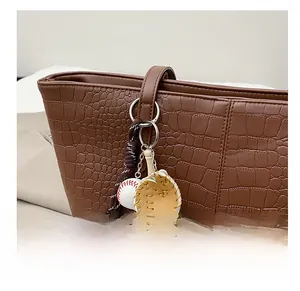 Detail of baseball glove and ball charm accessory on a brown alligator tote bag