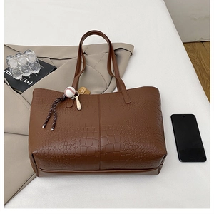 Close-up of brown crocodile texture tote bag with baseball charm on beige trench coat