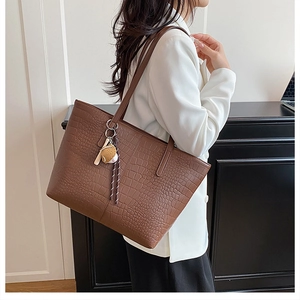Detail of a brown crocodile pattern leather tote bag with long handles and a cute charm