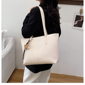 Detail of cream large tote bag with crocodile pattern and baseball charm accessory