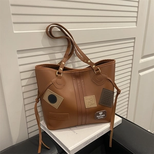 Caramel brown large tote bag with vintage patches and side tassels on a white stand