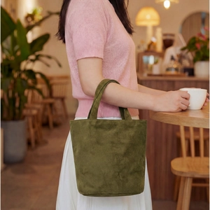 Dettaglio di una borsa tote in pelle scamosciata verde muschio tenuta da una modella