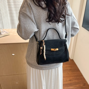 Retro black matte crossbody bag with gold buckle and beaded charm worn by a model