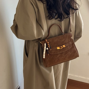Dark brown suede crossbody bag with gold buckle and beaded charm worn with a coat