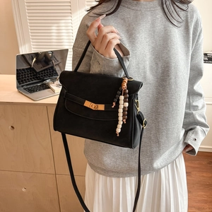 Detail of black matte retro handbag with gold lock and wooden bead strap on model