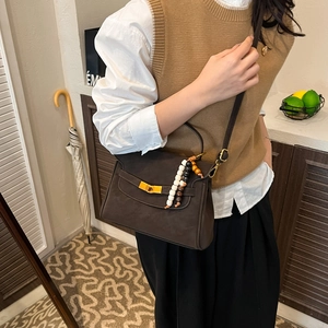 Detail view of deep brown frosted leather bag with metal buckle and beaded pendant accessory