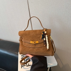 Detail of a brown matte handbag featuring a wooden bead charm and golden twist lock
