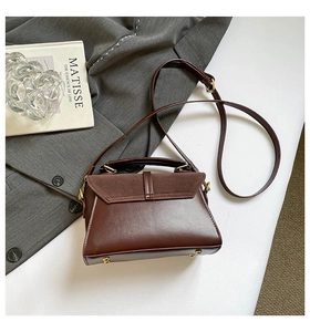 Détail du sac à main en cuir marron montrant les textures mixtes et les pieds en métal doré