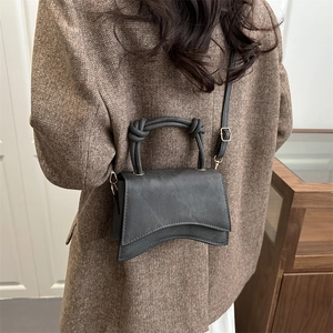 Chic dark grey matte leather handbag with curved base and knot handle on a model