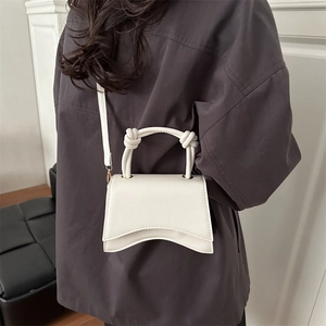 Minimalist white faux leather crossbody bag with curved base and knotted handle on model