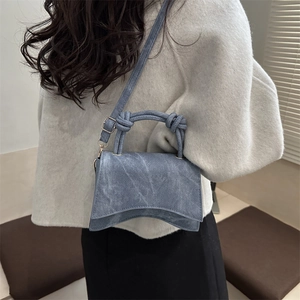 Vintage blue denim crossbody bag with woven knot handle and curved base on model