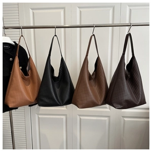 Detailed view of woven leather tote bags in four neutral colors hanging on a metal rack