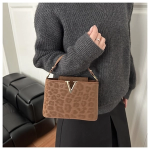 Close-up of leopard print suede handbag with gold V-shaped buckle and textured finish