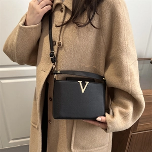 Minimalist black pebbled leather bucket bag with gold V-hardware on khaki wool coat
