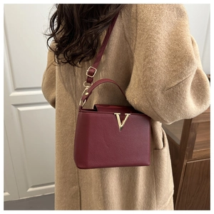 Detail of burgundy textured leather handbag with gold V-buckle on a camel wool coat