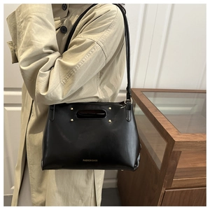 Detailed view of the black leather handbag featuring gold rivet accents and fashion text