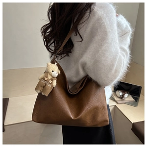 Detail of dark brown leather tote bag featuring a cute bear charm and large capacity