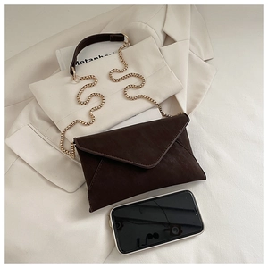 Detail of dark brown frosted leather envelope bag with gold chain and handle on a blazer