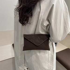 Minimalist matte dark brown crossbody envelope bag with gold chain strap worn by a model