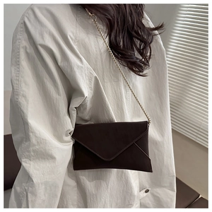 Detail of dark brown envelope crossbody bag with matte texture and golden chain strap