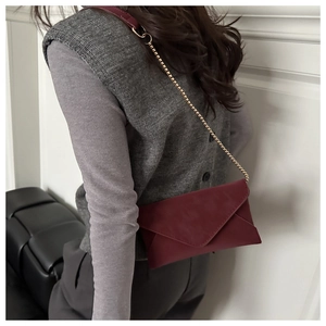 Detailed view of burgundy envelope crossbody bag with fine gold chain strap worn by model