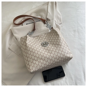 Detail of monogram tote bag with brown leather straps, chain detail and metallic M logo